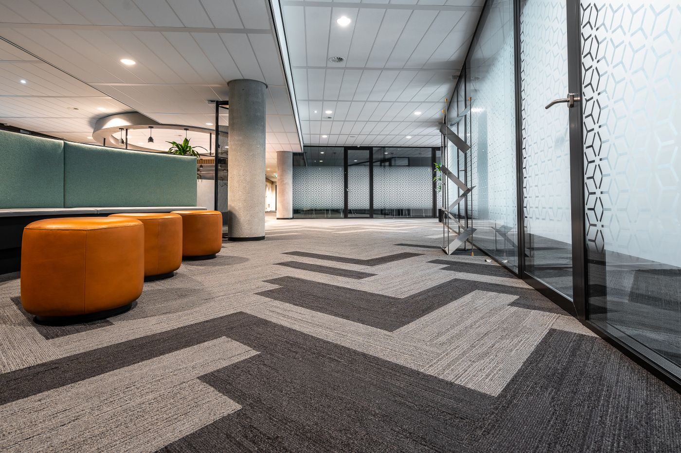 A modern office corridor with patterned commercial carpet running between glass-walled meeting rooms