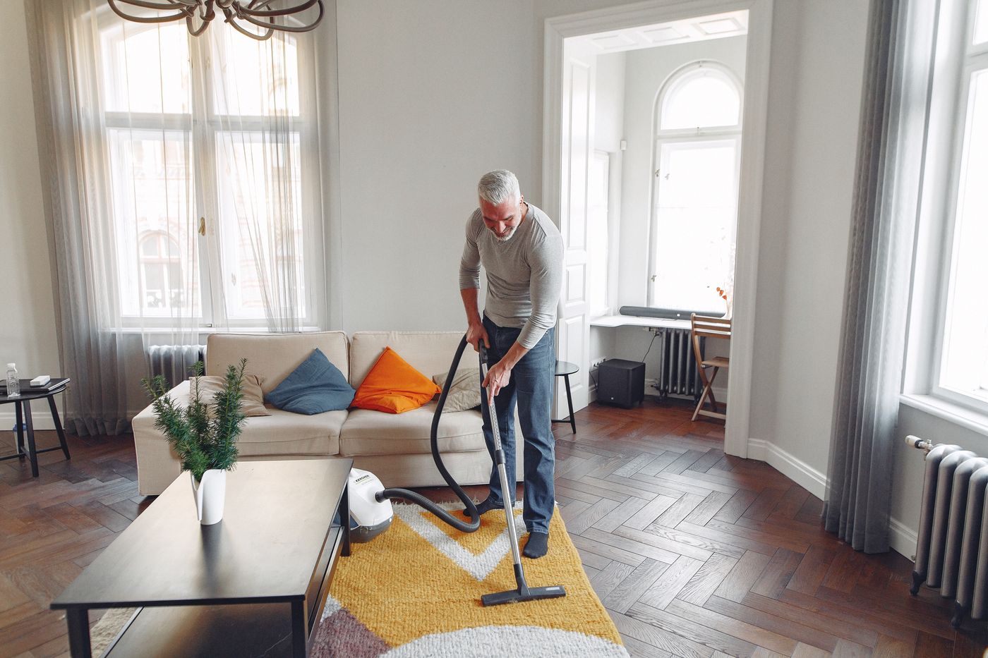 A man cleaning a living-room floor with an extractor, working the carpet in daylight
