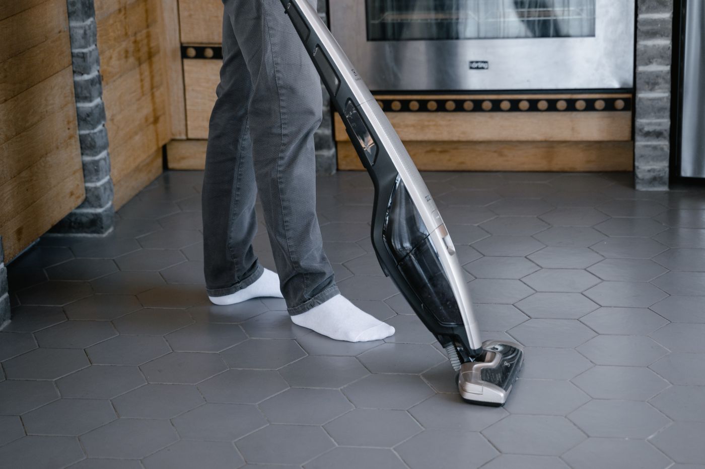 A person cleaning a tiled floor with a wet floor cleaner, working across the grout lines