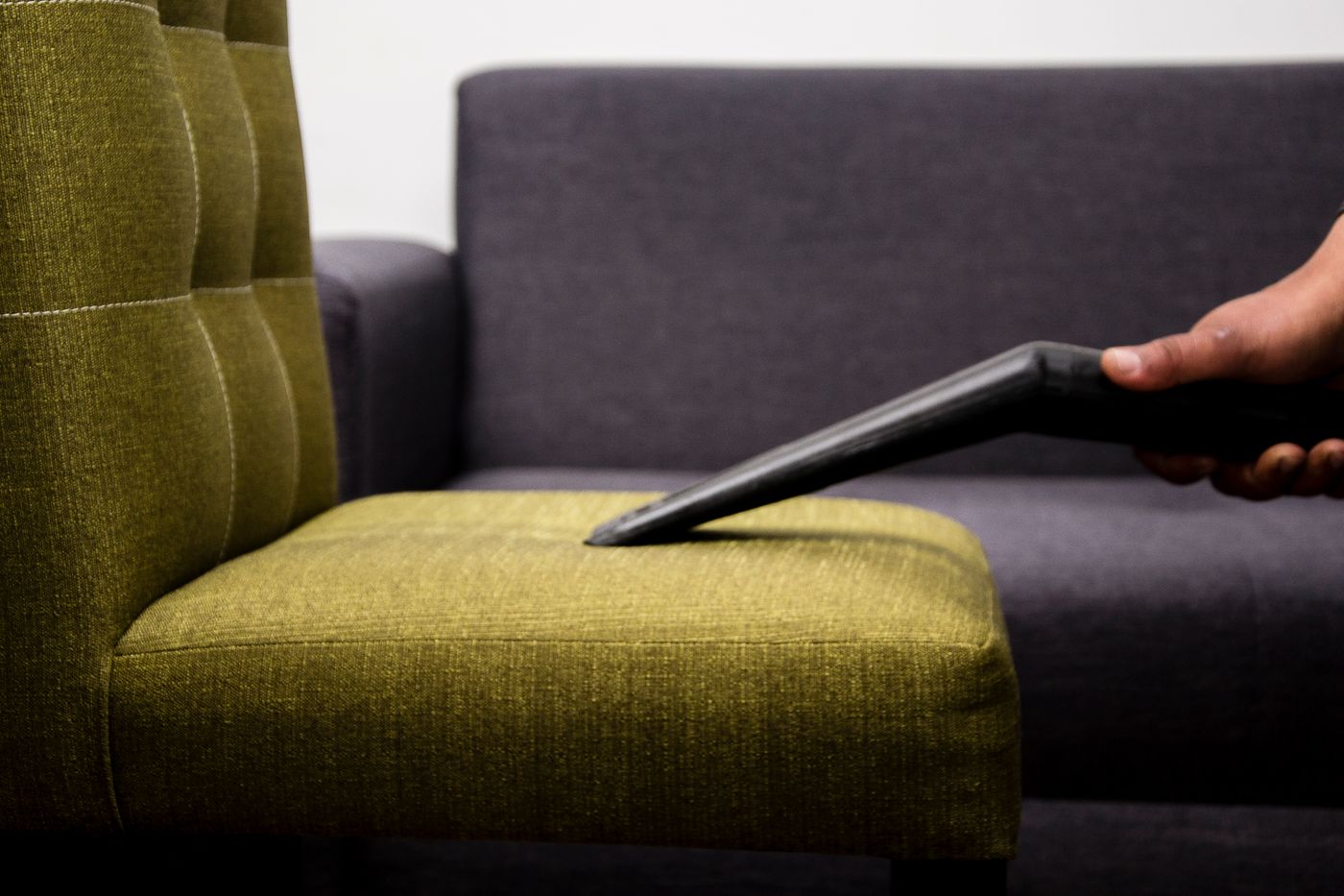 Close-up of an upholstery nozzle worked along the seam of a modern sofa chair